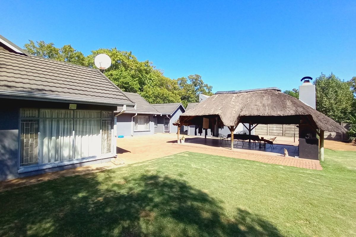 Spacious rear garden featuring a paved patio area with a thatched lapa and built-in braai, perfect for outdoor entertaining.