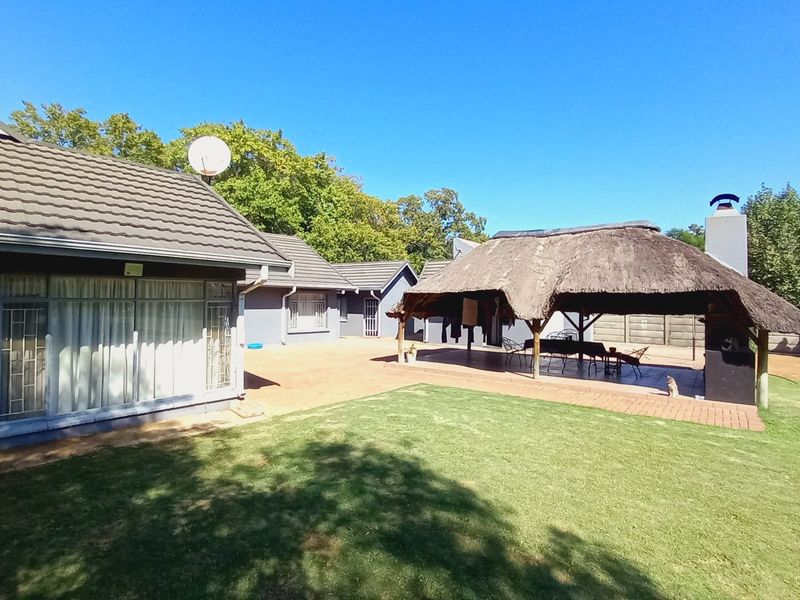 Spacious rear garden featuring a paved patio area with a thatched lapa and built-in braai, perfect for outdoor entertaining.