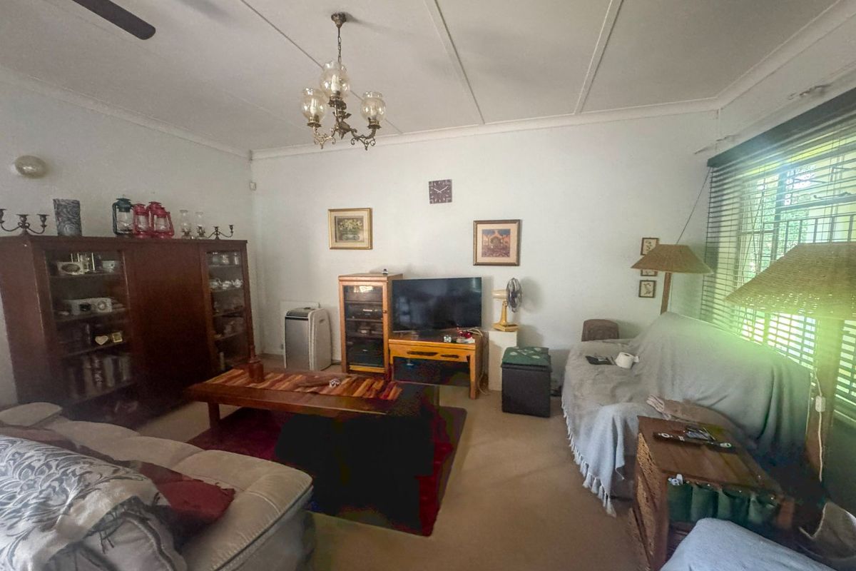 A living room featuring a ceiling fan, chandelier, and window blinds with security bars.