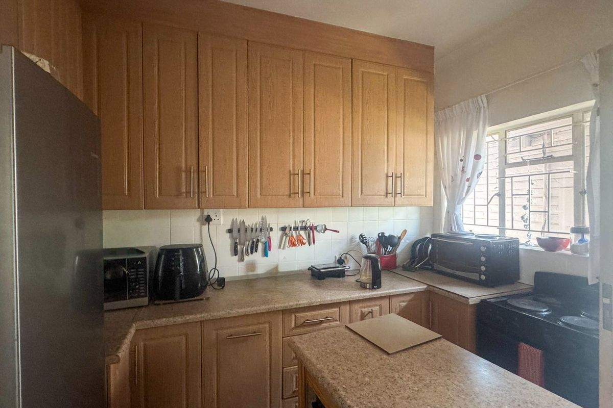 A functional kitchen featuring wood-look laminate cabinetry, durable countertops, a tiled backsplash, and a window with security bars for natural light.