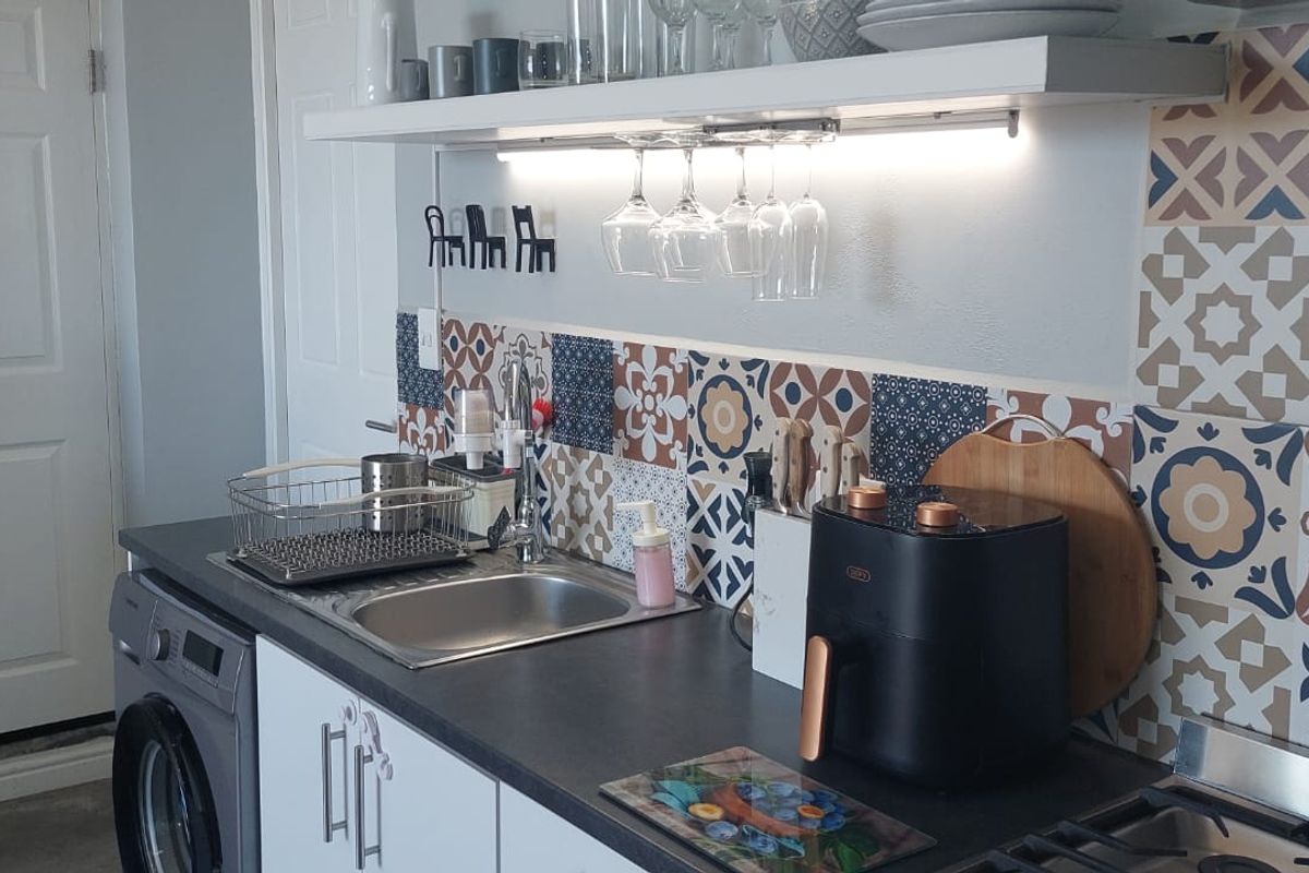 A well-maintained kitchen area featuring patterned tile splashbacks, modern cabinetry, integrated laundry appliances, and functional under-shelf lighting.