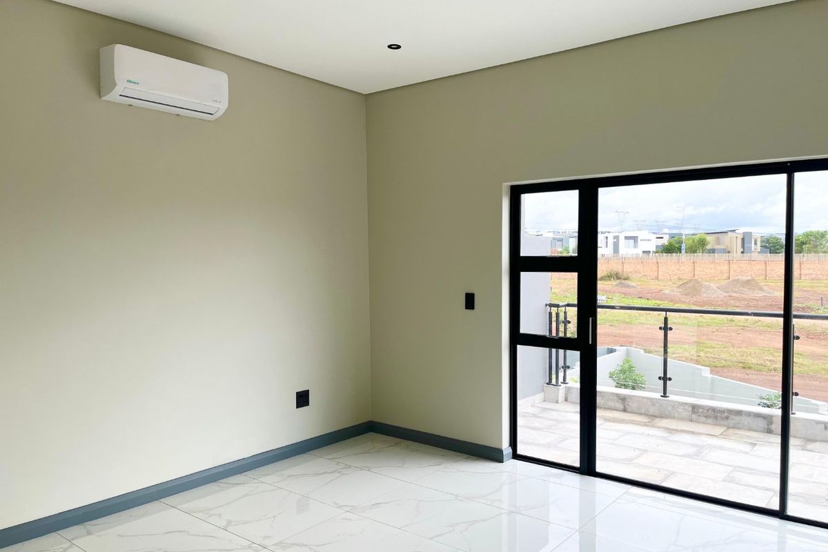 A bright, modern bedroom featuring polished marble-look floor tiles, a wall-mounted air conditioning unit, and a sliding glass door leading to a private balcony.