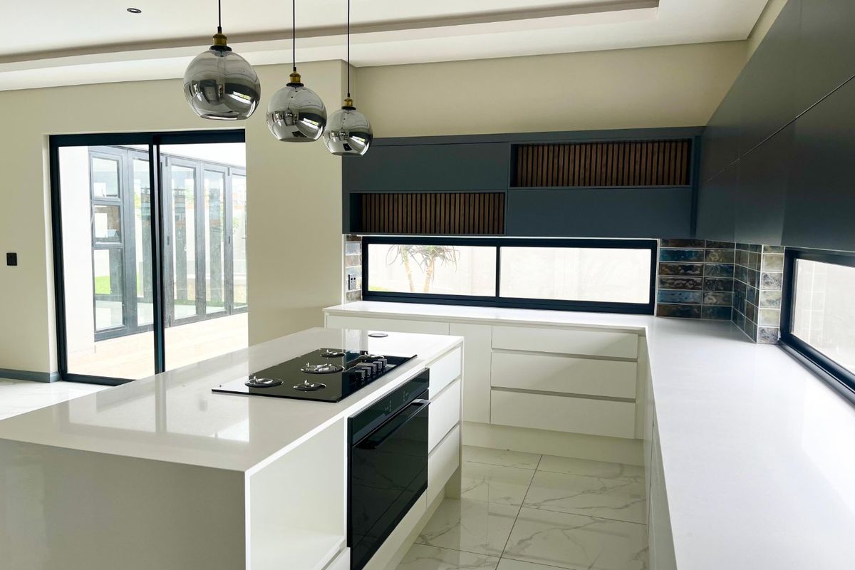 Modern kitchen featuring a central island with built-in oven and gas hob, sleek cabinetry, quartz countertops, and large sliding doors leading to the outdoors.
