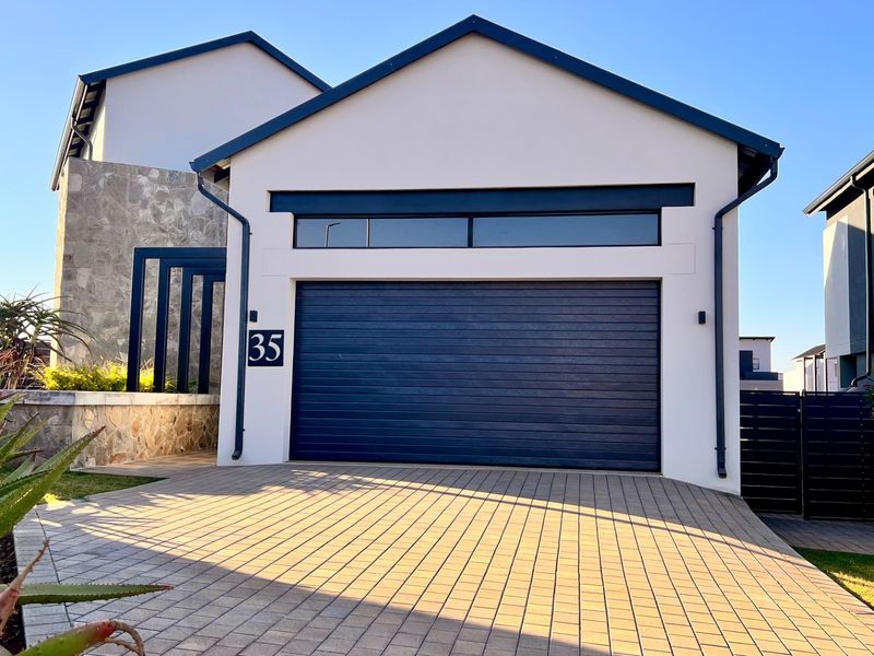 Modern front elevation featuring a paved driveway, stone cladding accents, and a sleek automated garage door with a clerestory window above.