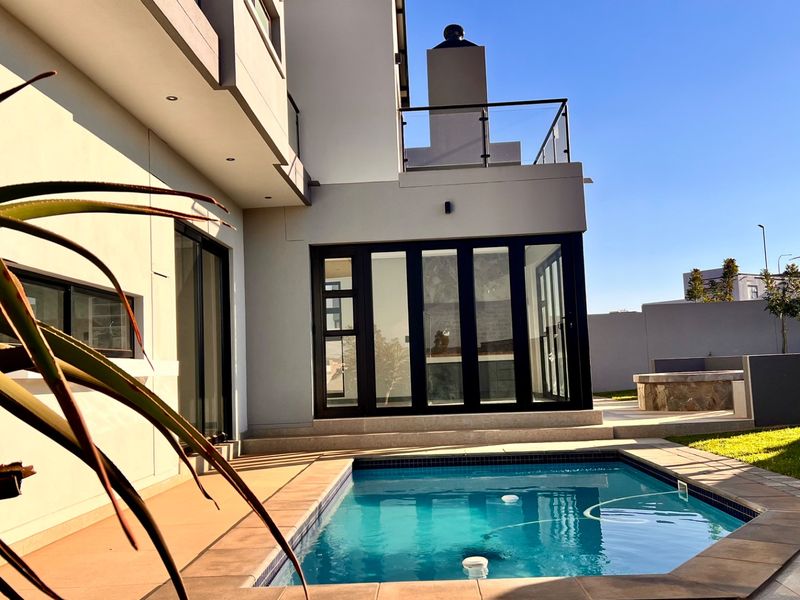 Modern outdoor entertainment area featuring a swimming pool, tiled patio, and an external fireplace, seamlessly connected to the home via large glass sliding doors.