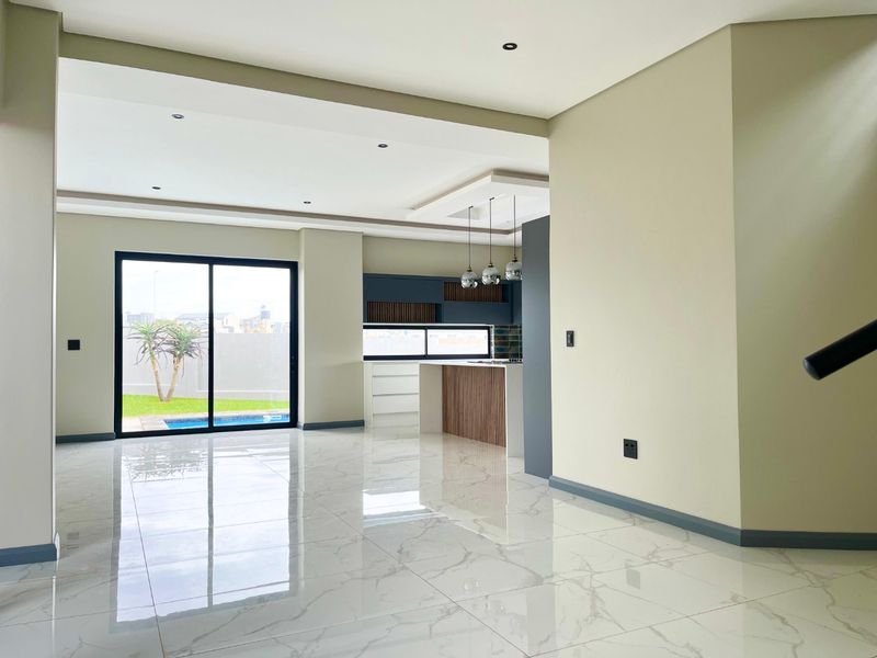 Spacious open-plan living and kitchen area featuring modern porcelain tile flooring, recessed lighting, and large sliding doors leading to the outdoor pool area.