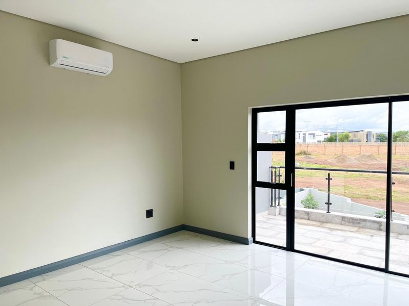 A bright, modern bedroom featuring polished marble-look floor tiles, a wall-mounted air conditioning unit, and a sliding glass door leading to a private balcony.