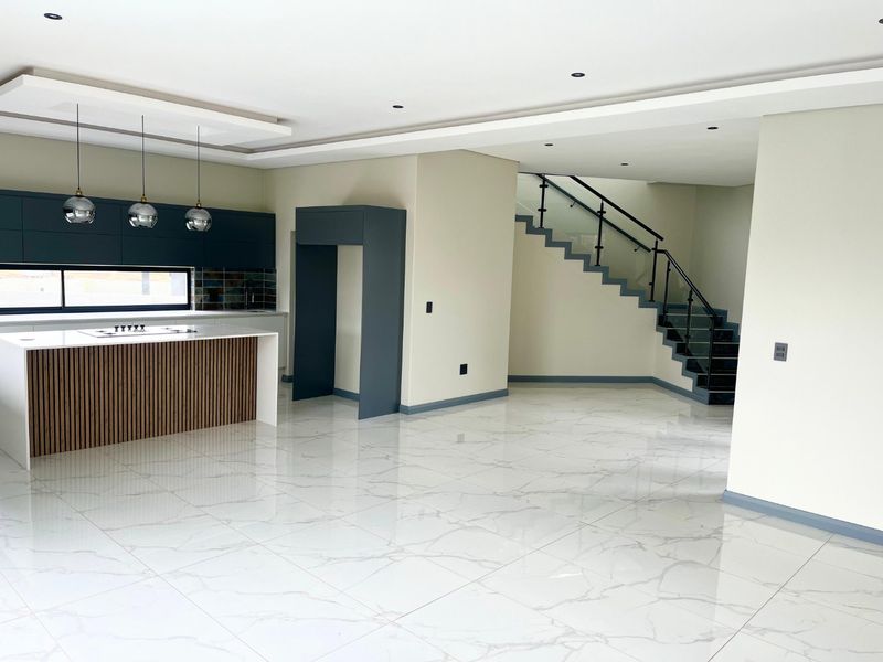 Modern open-plan kitchen featuring a central island, sleek cabinetry, and a striking staircase with glass balustrades, set against polished marble-look flooring.
