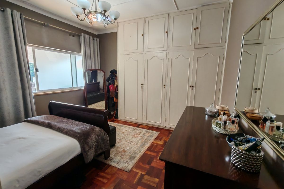 A well-maintained bedroom featuring classic parquet flooring, extensive built-in cabinetry, and a traditional ceiling light fixture.
