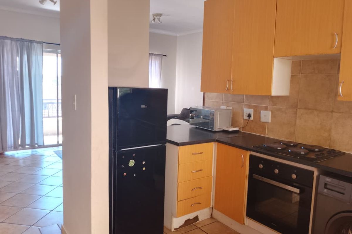 A compact kitchen featuring laminate cabinetry, tiled backsplash, and built-in oven with electric hob, showing signs of wear on the lower cabinet base.