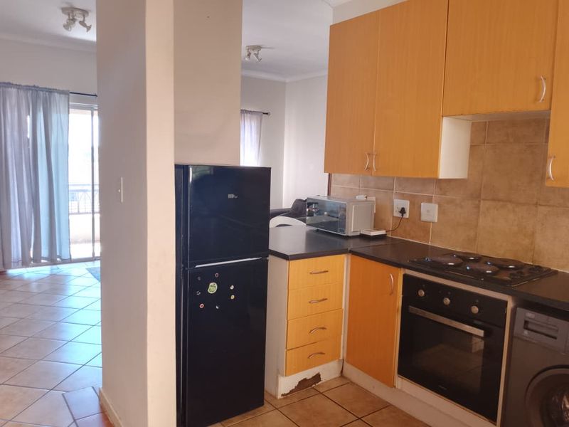 A compact kitchen featuring laminate cabinetry, tiled backsplash, and built-in oven with electric hob, showing signs of wear on the lower cabinet base.