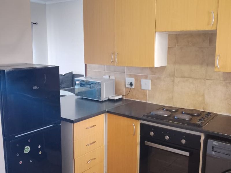 Compact kitchen featuring light wood-tone cabinetry, built-in oven, electric hob, and tiled backsplash, requiring minor repairs to the lower cabinet base.