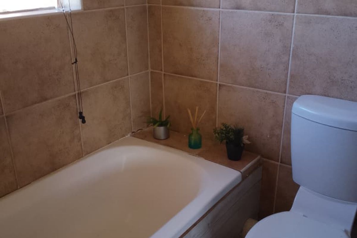 A functional bathroom featuring a bathtub, toilet, and neutral wall tiling, offering a practical layout with potential for modern updates.