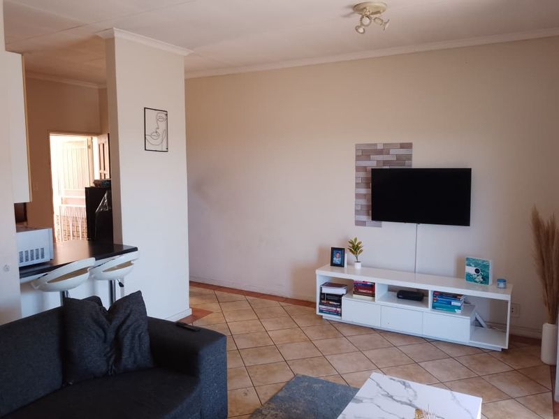 Open plan living area featuring tiled flooring, a breakfast counter, and a decorative feature wall section for television mounting.