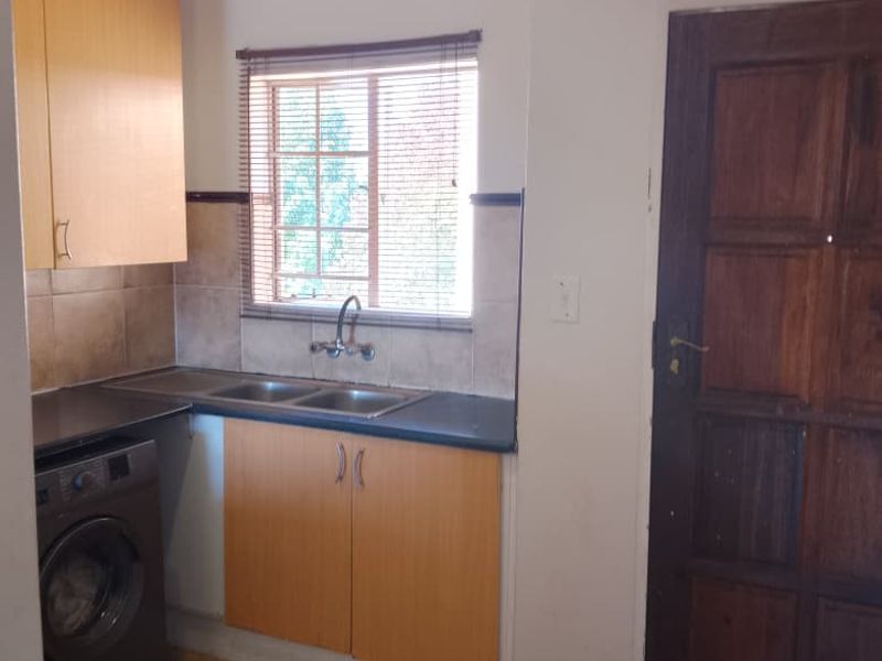 A functional kitchen area featuring laminate cabinetry, a double basin sink, tiled backsplash, and tiled flooring, with direct access via a timber door.
