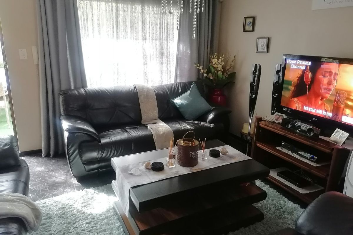 A comfortable living room featuring tiled flooring, large window with curtain tracks, and access to an outdoor area.