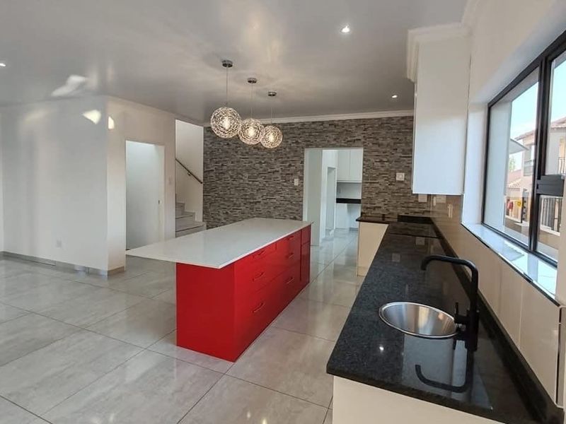 Modern open-plan kitchen featuring a vibrant red island, stone feature wall, sleek dark countertops, and large format floor tiles in a bright, spacious layout.