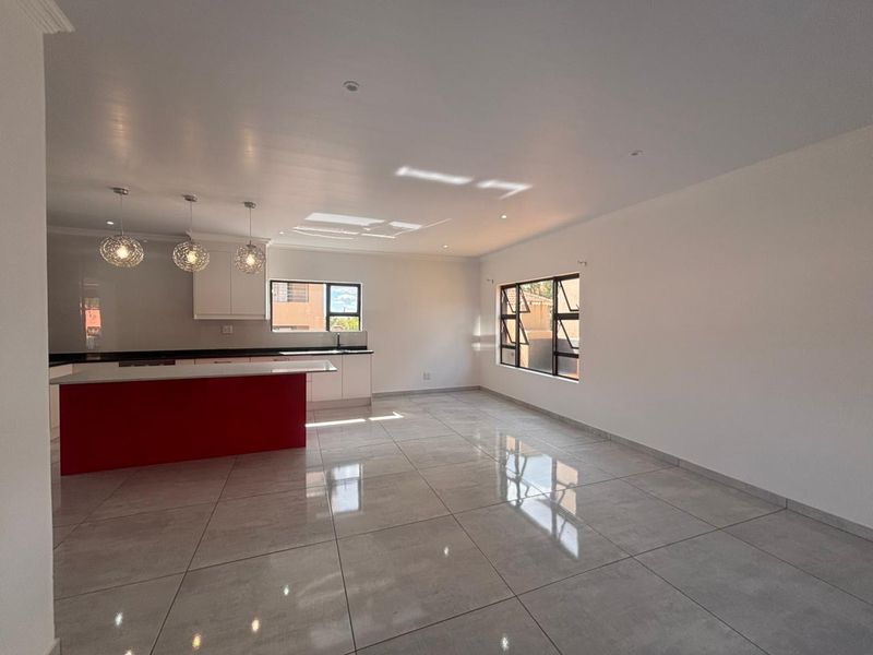 Spacious open-plan living and kitchen area featuring modern tiled flooring, a central island, and ample natural light through large windows.