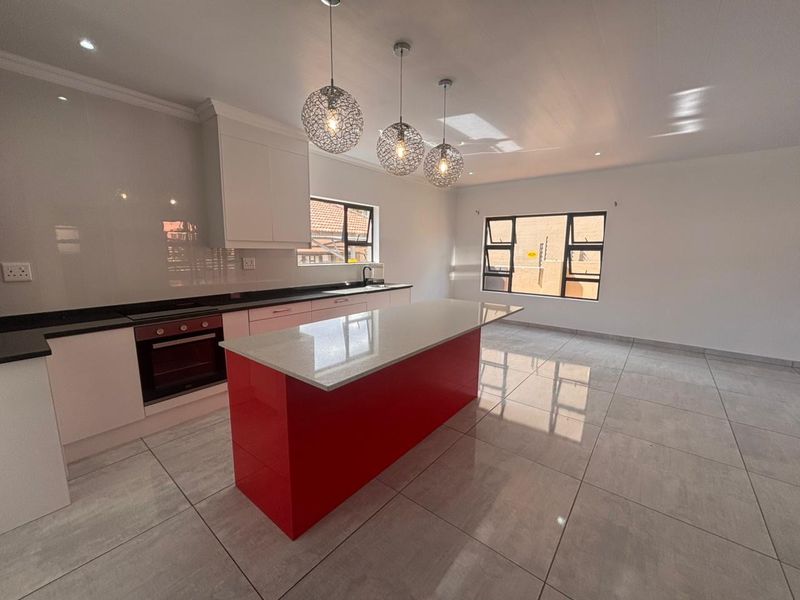 Modern kitchen featuring a vibrant red island, sleek quartz countertops, built-in oven, and high-gloss cabinetry in an open-plan layout with tiled flooring.