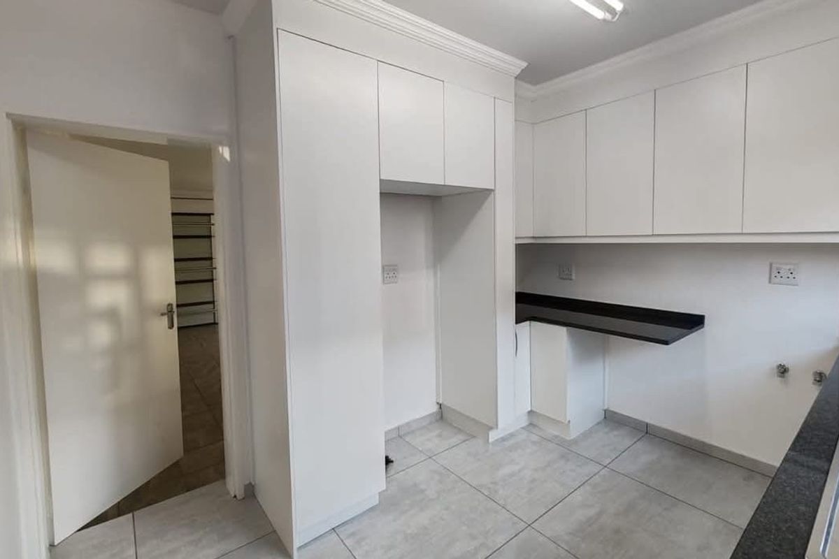 A clean, modern kitchen featuring white cabinetry, dark stone countertops, and neutral tiled flooring, offering a functional and well-maintained space.