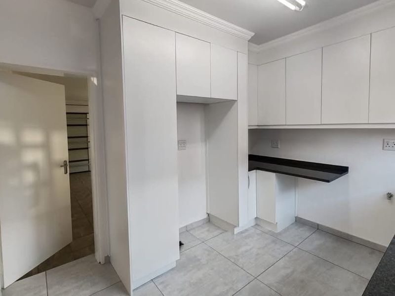 A clean, modern kitchen featuring white cabinetry, dark stone countertops, and neutral tiled flooring, offering a functional and well-maintained space.