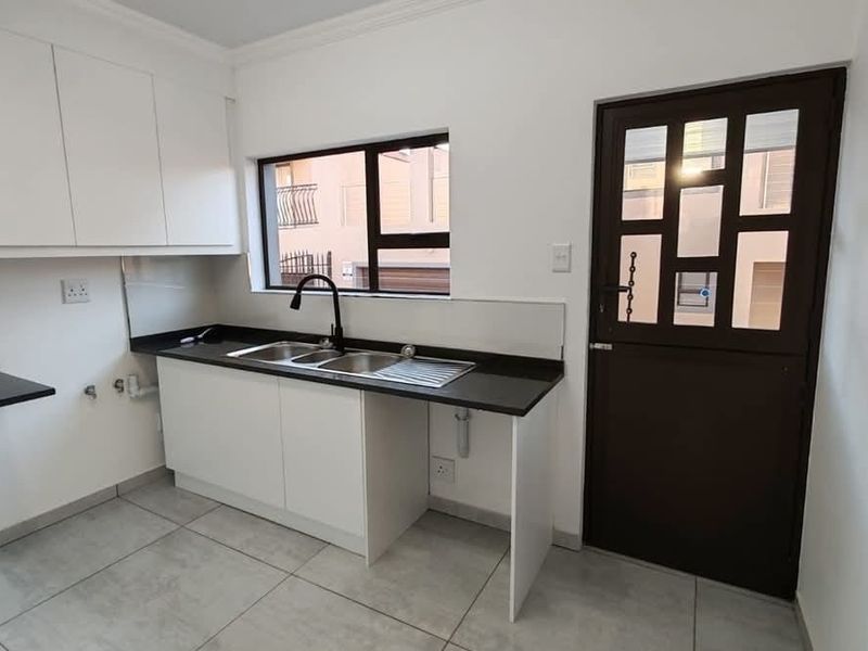 A clean, modern scullery featuring white cabinetry, dark stone countertops, a double sink with a black mixer tap, and tiled flooring.