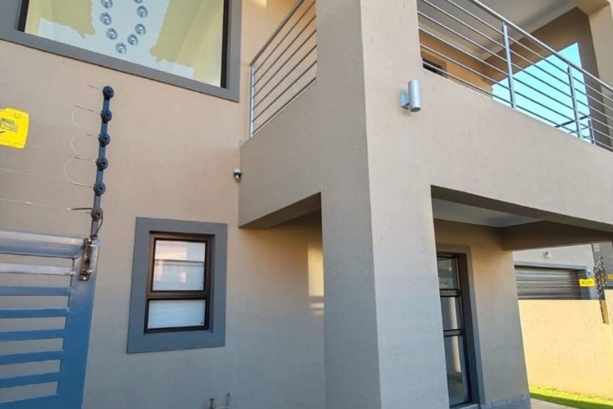 A well-maintained rear exterior view featuring a covered patio, stainless steel balustrades on the balcony, and secure perimeter electric fencing.