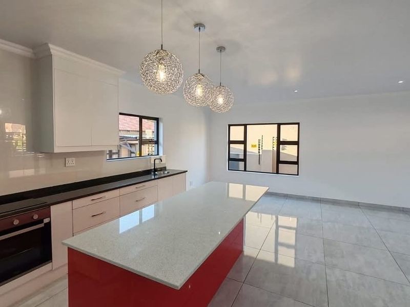 Modern open-plan kitchen featuring a central island, stone countertops, built-in oven, and sleek tiled flooring in a bright, contemporary space.