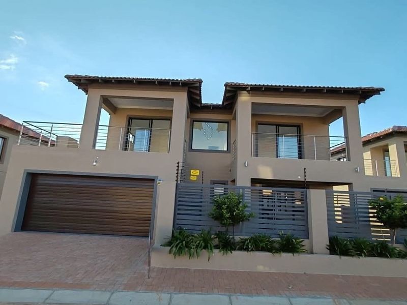 Modern double-story residential facade featuring a double garage, upper-level balconies with stainless steel balustrades, and secure perimeter fencing.