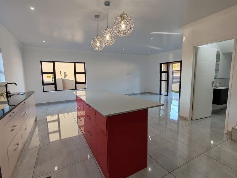 Modern open-plan kitchen featuring a vibrant red island with quartz countertops, high-gloss cabinetry, and polished porcelain floor tiles in a bright, spacious layout.