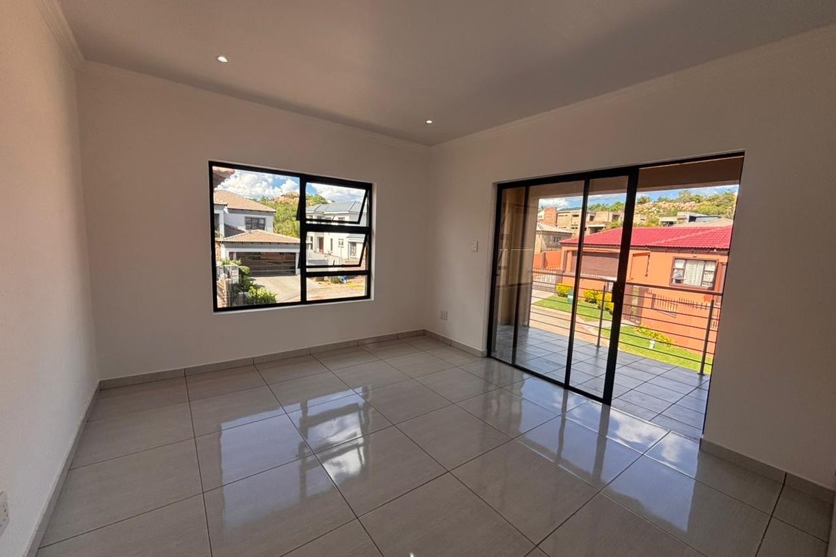 A bright, empty living area featuring neutral tiled flooring, modern aluminium window frames, and sliding doors leading to an outdoor patio space.