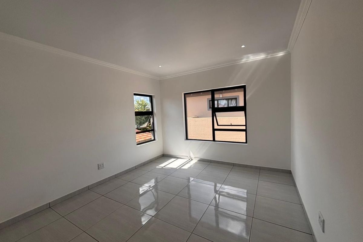 A bright, empty bedroom featuring neutral tiled flooring, modern aluminium window frames, and recessed downlighting, offering a clean and versatile living space.