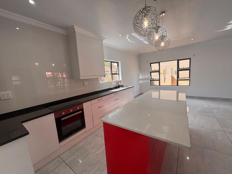 Modern kitchen featuring a central island, stone countertops, built-in oven, and sleek cabinetry, finished with large format floor tiles and contemporary lighting.