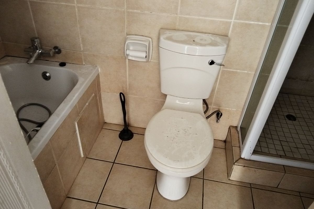 A functional bathroom featuring a bathtub, separate shower enclosure, and tiled finishes, requiring deep cleaning and cosmetic updates to improve its overall condition.