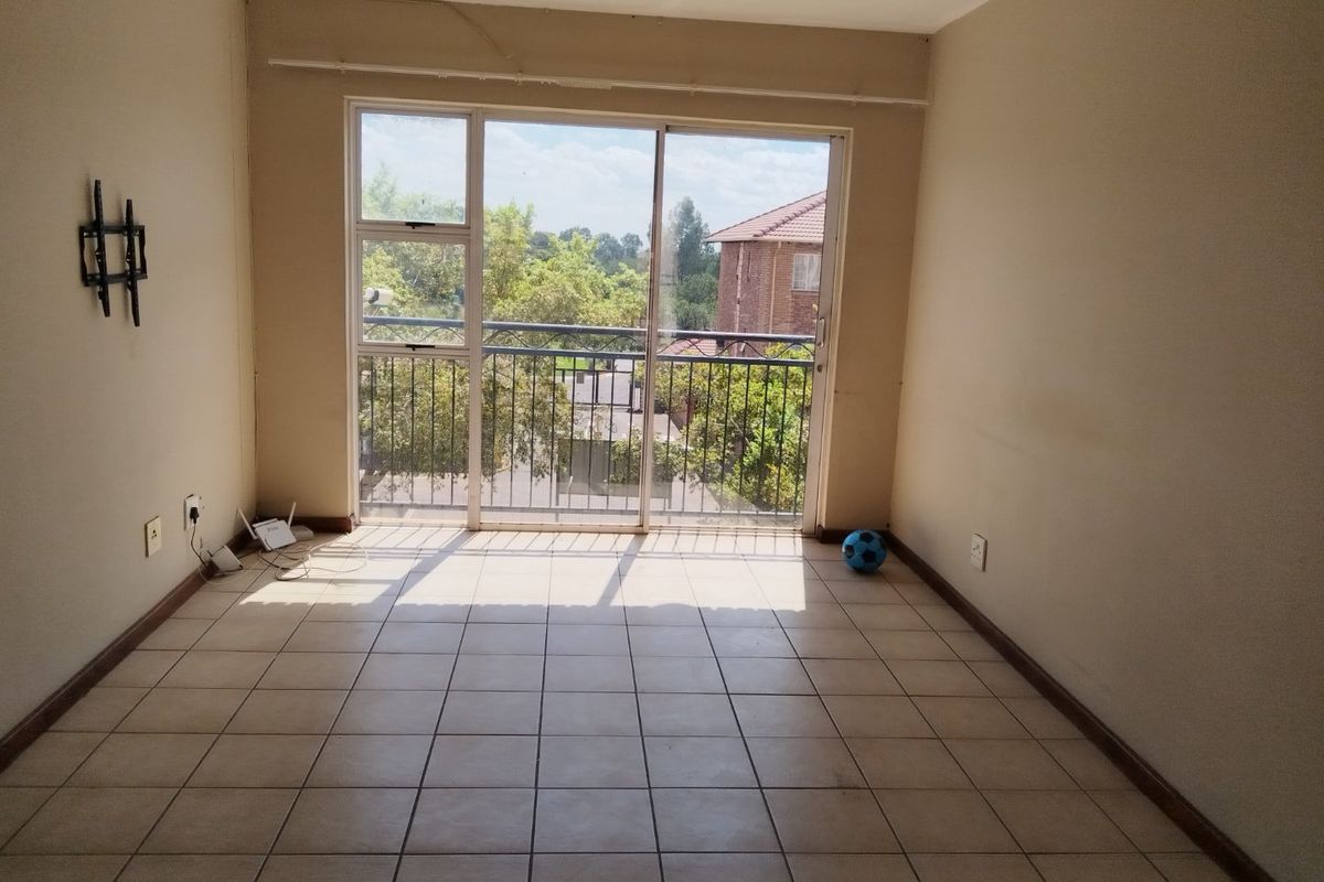 An empty living room featuring tiled flooring and a large sliding glass door that provides access to a balcony with neighborhood views.