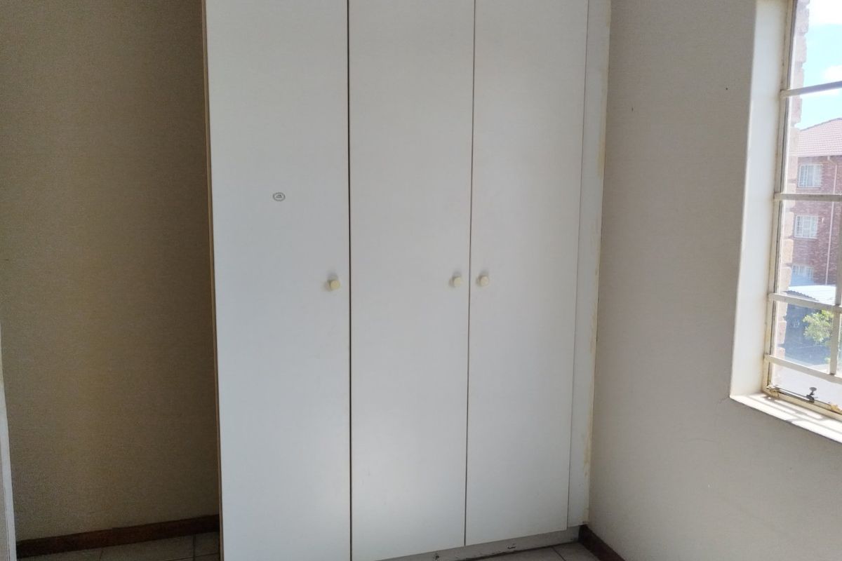 A bedroom featuring a built-in wardrobe, tiled flooring, and a window with security bars, presenting a blank canvas for potential updates.