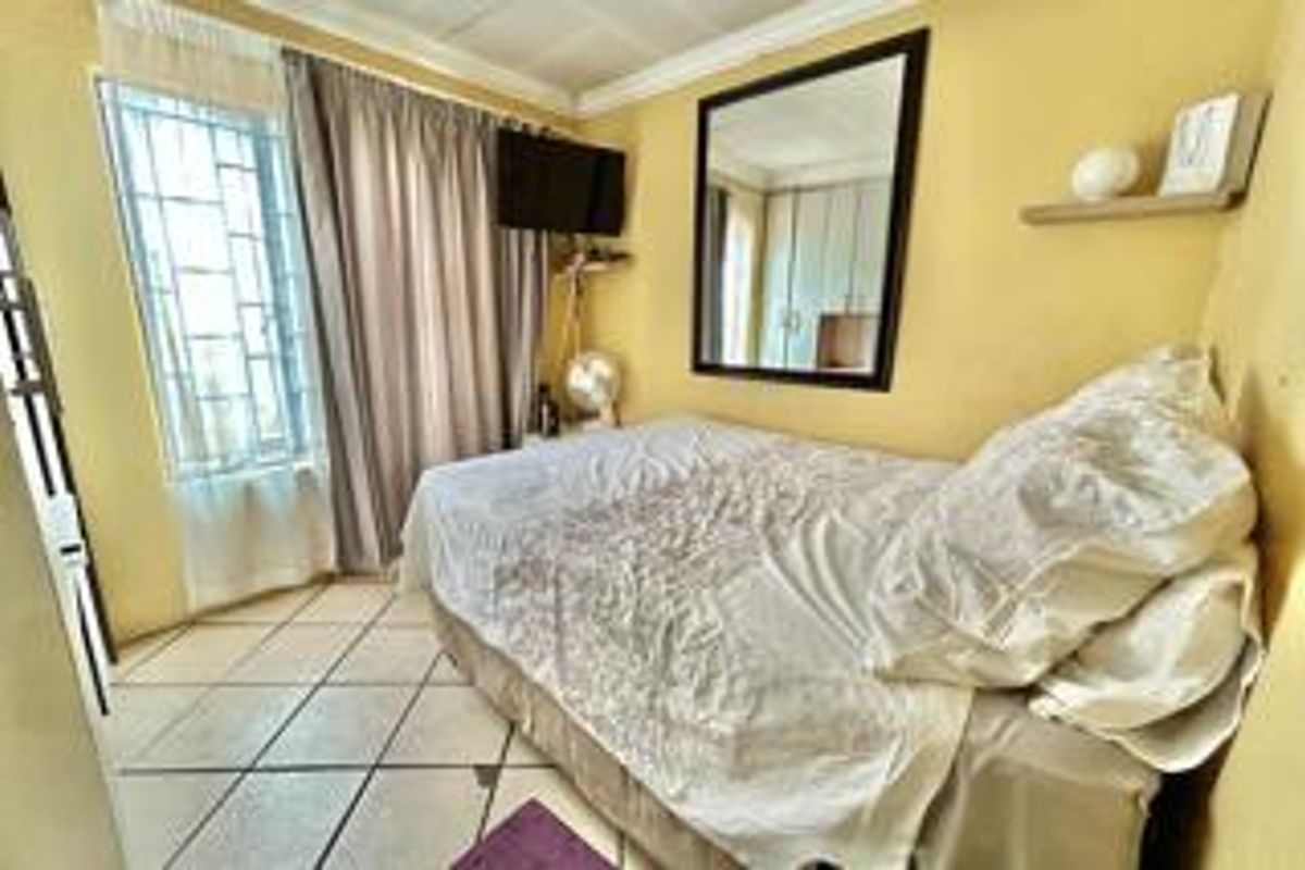 A compact bedroom featuring tiled flooring, security bars on the window, and ceiling cornice detailing.