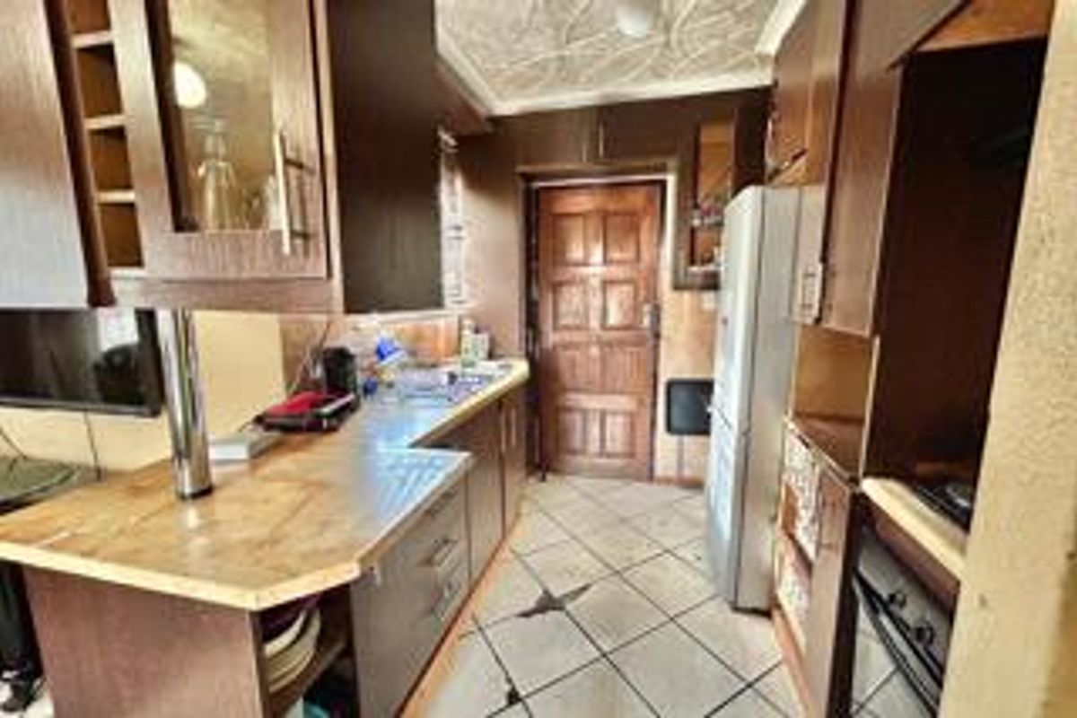 A dated kitchen featuring wood-tone cabinetry, laminate countertops, and tiled flooring, offering potential for a modern renovation.