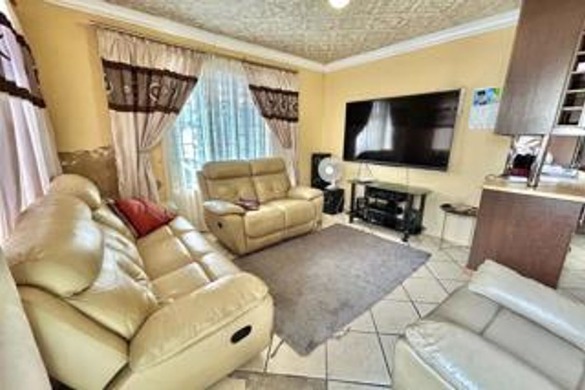 A living room featuring tiled flooring and a textured ceiling, with visible wear on the wall finish near the window area.