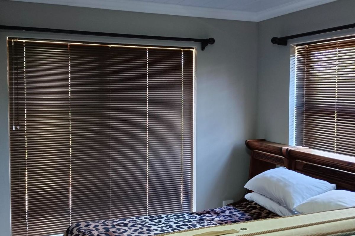 A bedroom featuring neutral wall tones, fitted venetian blinds, and a built-in wardrobe, offering a functional and private living space.