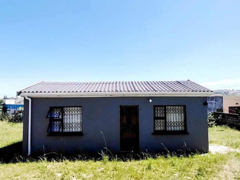 A front exterior view of a single-story residential house featuring a corrugated metal roof, security gates, and casement windows set on a grassed plot.