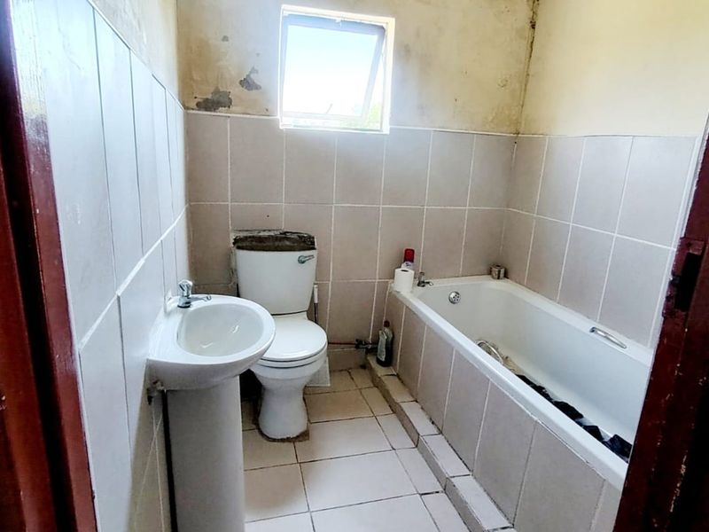A compact bathroom featuring a pedestal basin, toilet, and bathtub with tiled finishes, currently requiring cosmetic renovation and wall repairs.