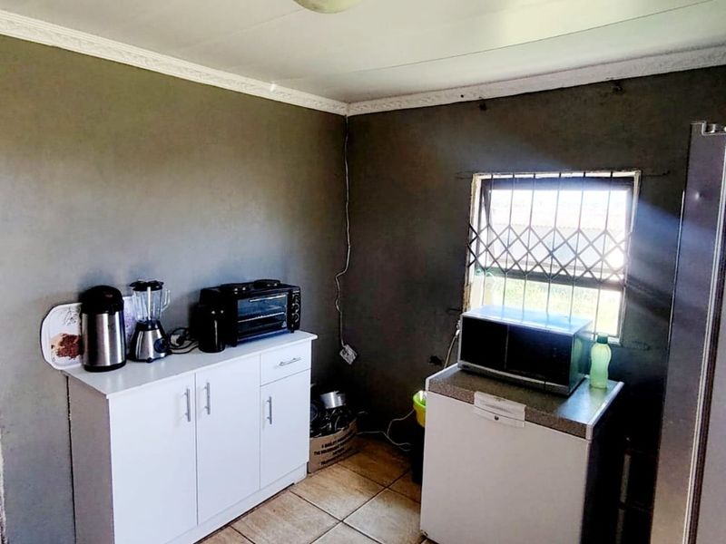 A compact kitchen area featuring tiled flooring, security bars on the window, and basic cabinetry, currently used as a functional prep space.