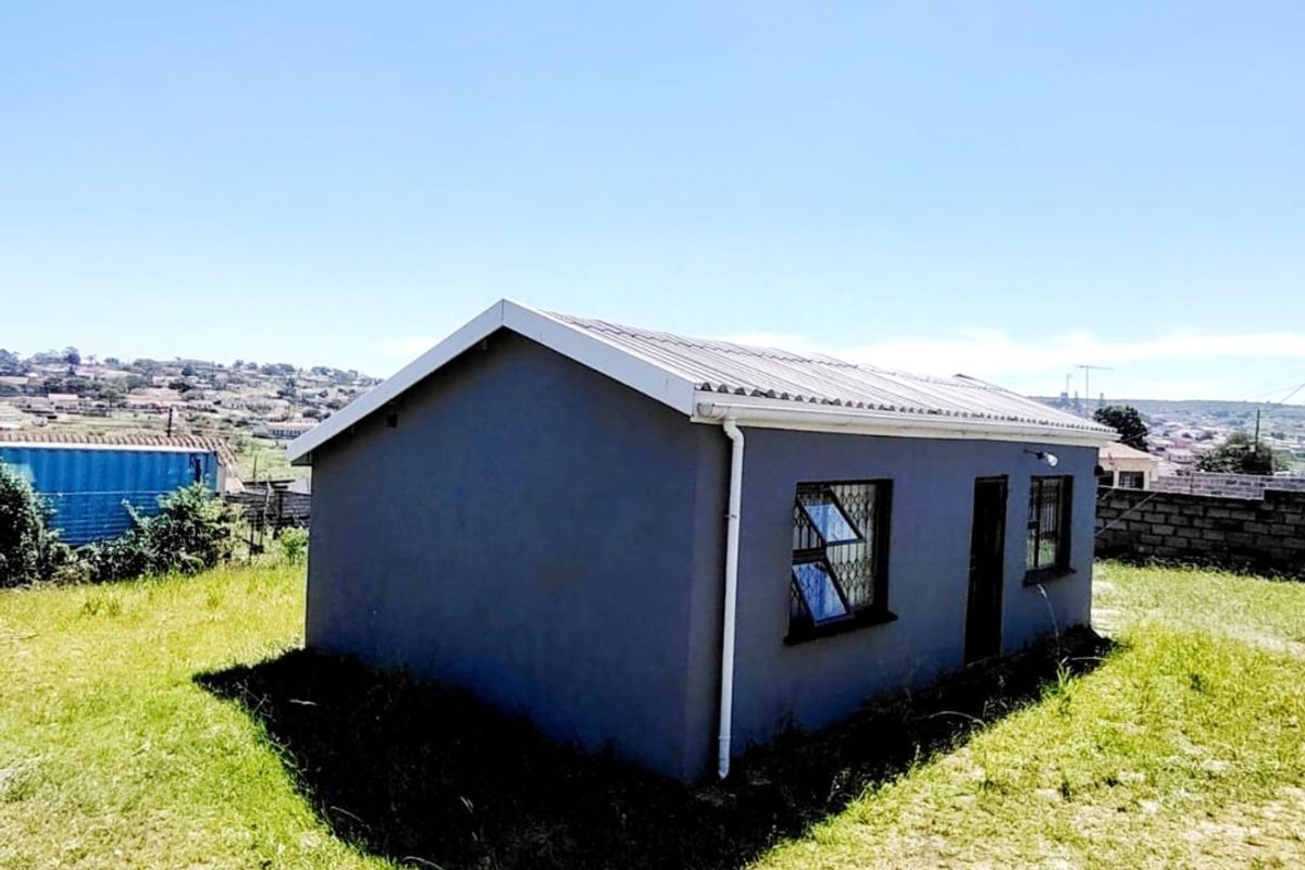 A detached structure with a grey exterior, corrugated metal roof, and security bars on the windows, situated on an open grassed plot.
