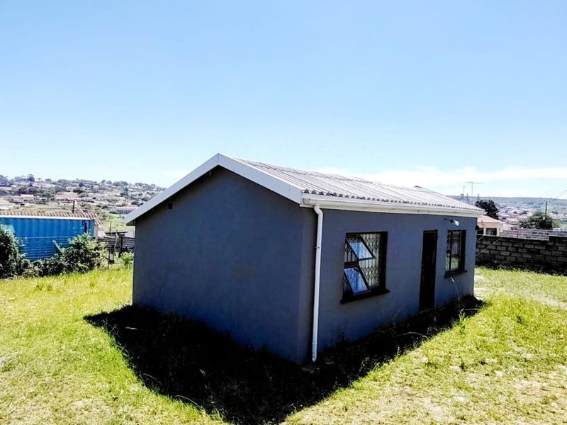 A detached structure with a grey exterior, corrugated metal roof, and security bars on the windows, situated on an open grassed plot.