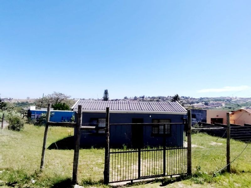 A detached single-story house featuring a corrugated metal roof and security bars, set within a fenced plot with an unmaintained garden area.