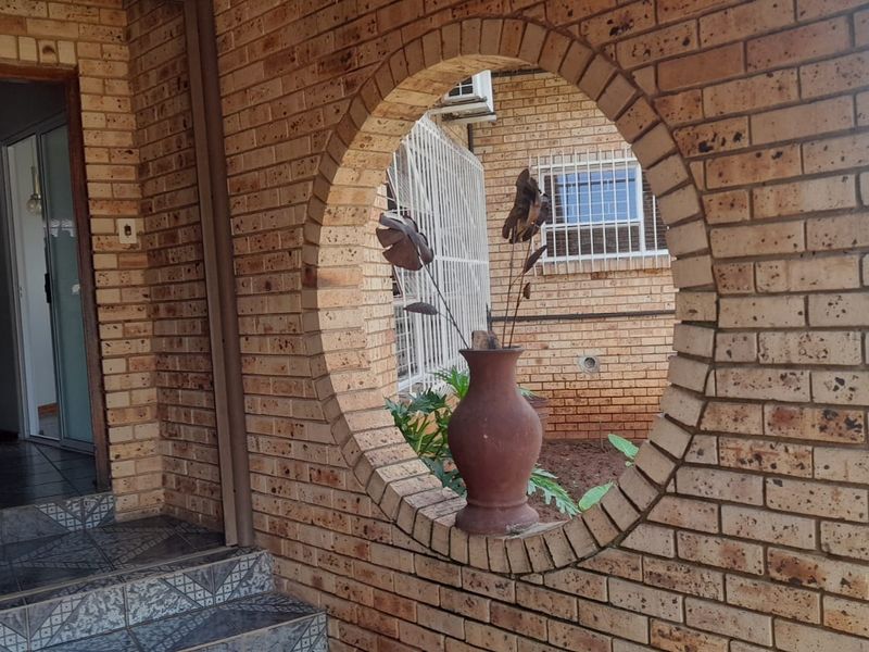 Covered patio area featuring a distinctive circular brick opening, tiled steps, and security features, providing access to the home's interior.