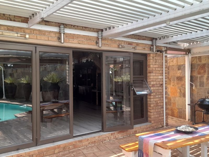 Covered patio area featuring a louvre roof, aluminium stacker doors, and a combination of facebrick and stone cladding finishes.