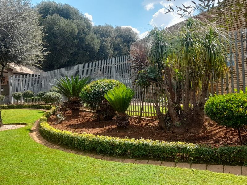 A well-maintained garden area featuring manicured lawn, established shrubs, and secure perimeter fencing with brick wall accents.