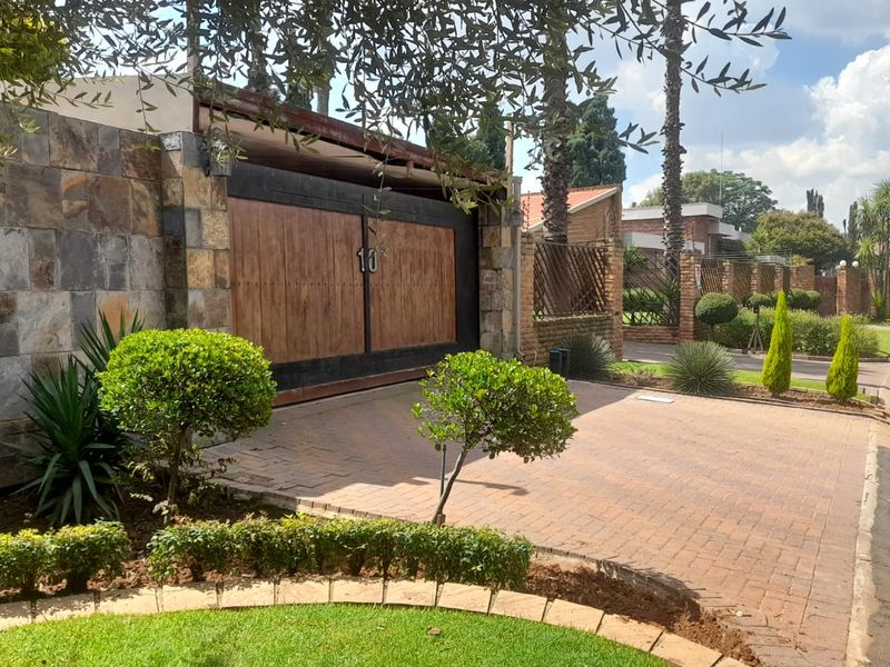 Front exterior view of the property featuring a paved driveway, stone-clad wall, and a large wooden garage door entrance.